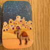 A hand-painted scene of a desert city under a starry night featuring a donkey in the foreground.