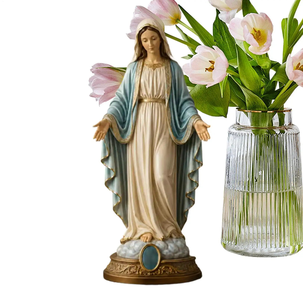 A religious figurine of the Blessed Mother with a halo, draped in blue and white robes, standing in front of pink tulips.