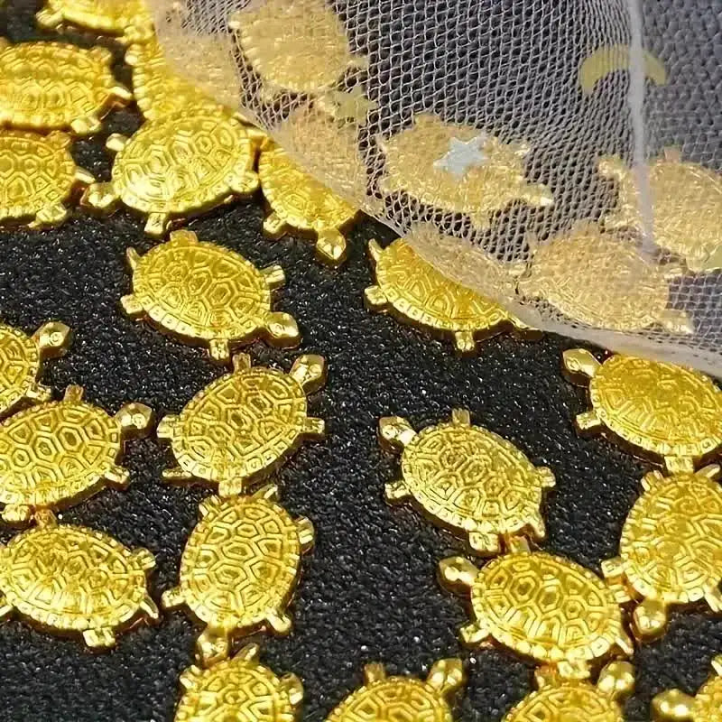 Goldene Geld-Schildkrötenfiguren verstreut auf dunker Oberfläche mit feinem Goldnetz.