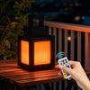 A hand holds a black pixel style RGB night light lantern glowing orange on a wooden deck.