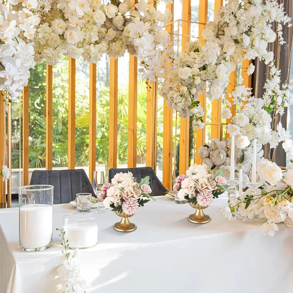 A white table setting with floral centerpieces featuring pink and cream roses under a chandelier of white flowers.