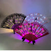 Pink and purple LED dancing hand fan with floral patterns illuminated in a dark setting.