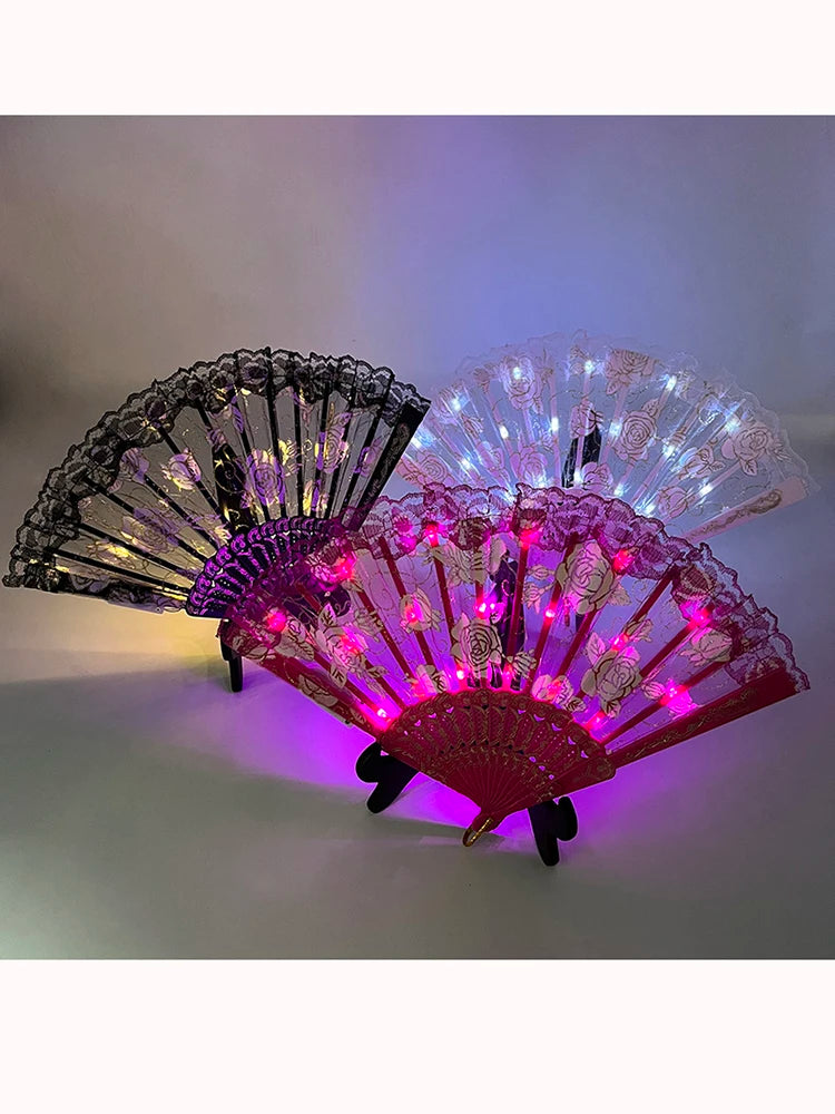 Pink and purple LED dancing hand fan with floral patterns illuminated in a dark setting.
