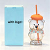 A clear glass coffee cup with an orange handle and a decorative floral collar sits next to its light blue packaging box.