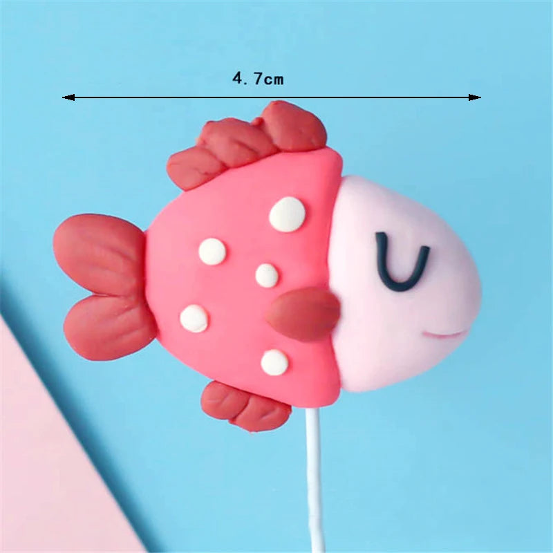 Pink and white edible cake toppers of various ocean animals including a crab, turtle, octopus, whale, starfish, and shell.