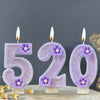 Three purple sparkling number candles 520 with purple flowers on a wooden surface