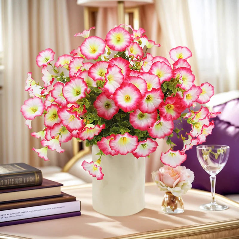 A bouquet of artificial silk cloth flowers in shades of pink and red displayed in a white vase on a table.
