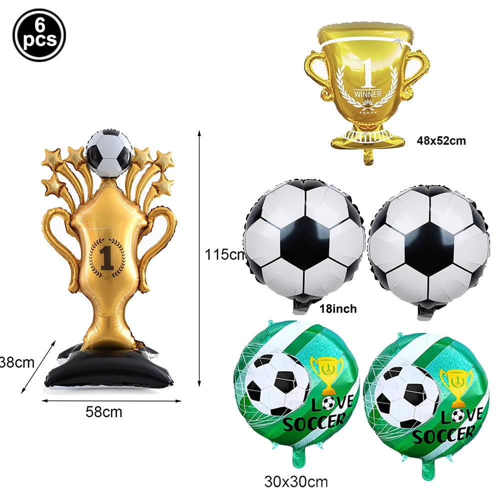 A set of gold and green soccer-themed party décor including a trophy, a football, and two soccer balls.