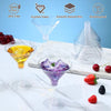 A set of clear plastic martini glasses with stems and a bottle of purple cocktail on a marble surface.