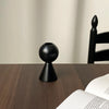 A black wooden candle holder with a tapered base and a decorative finial sits on a dark wooden surface.
