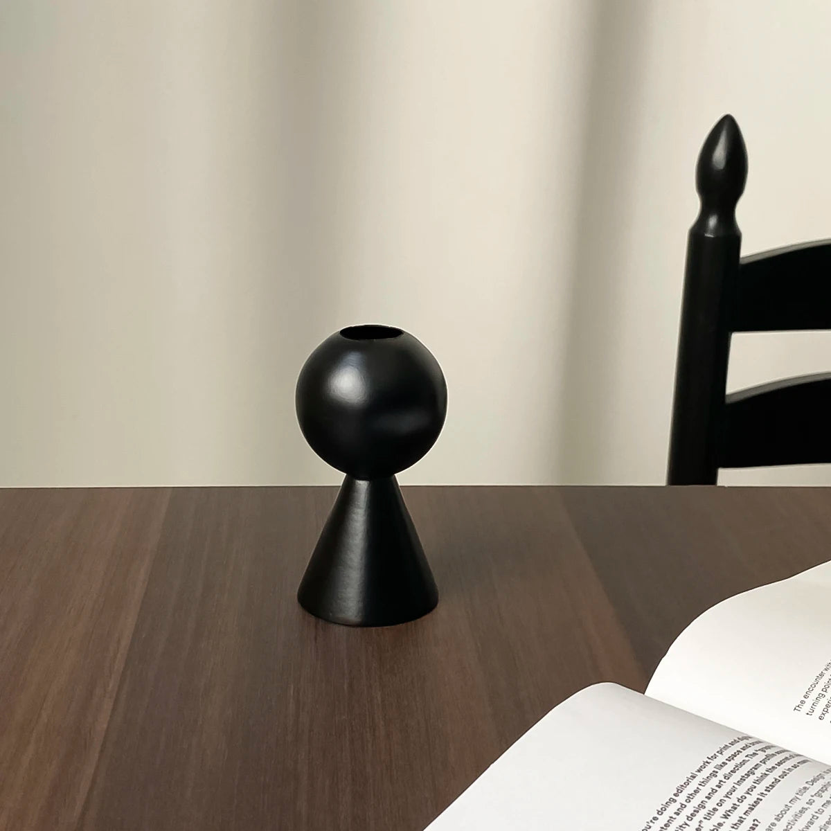 A black wooden candle holder with a tapered base and a decorative finial sits on a dark wooden surface.