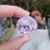A hand holds a round, faceted pink crystal ice crack ball used as water fountain decor.