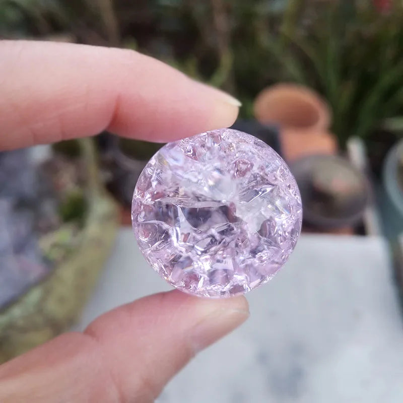 A hand holds a round, faceted pink crystal ice crack ball used as water fountain decor.