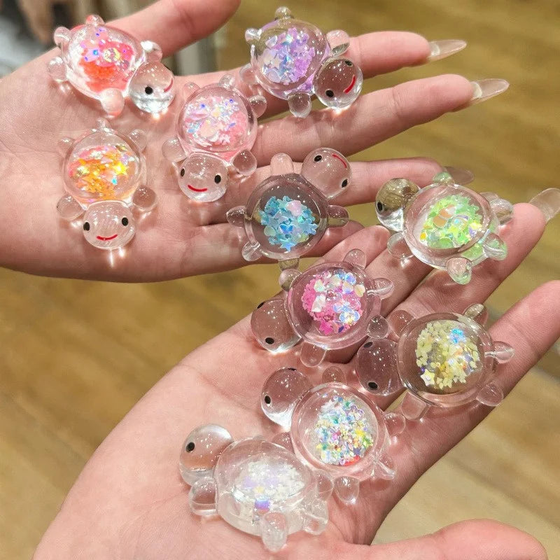 A hand holds several glow-in-the-dark mini sea turtle figurines with colorful glitter for DIY crafts.