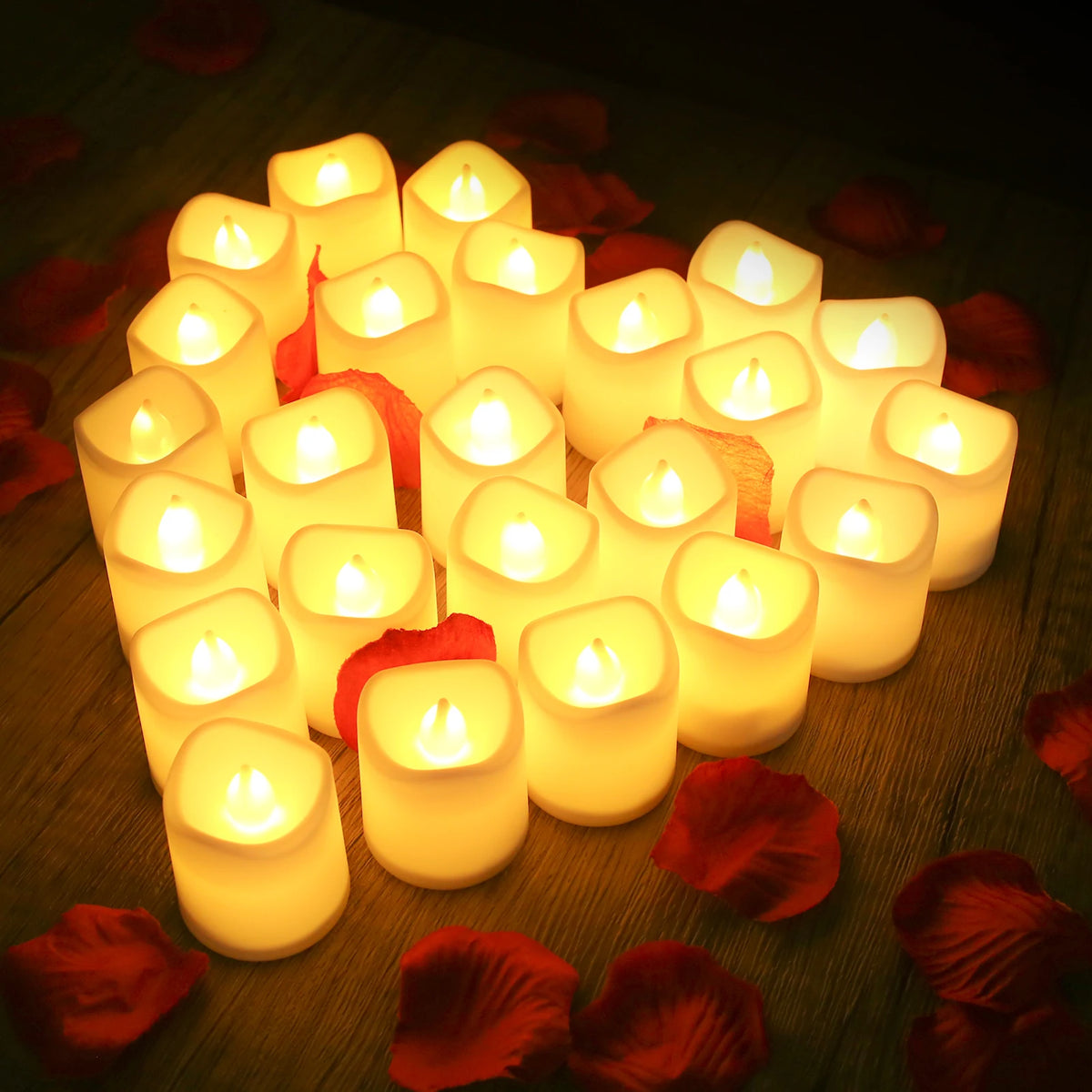 A cluster of glowing white votive tea lights arranged on a dark wooden surface surrounded by red rose petals.