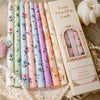 A set of French printed pole candles in various pastel colors displayed on a lace cloth.