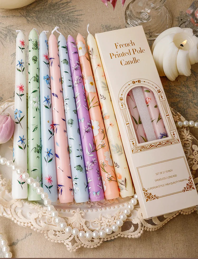 A set of French printed pole candles in various pastel colors displayed on a lace cloth.