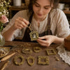 A woman is crafting a set of vintage gold resin mini photo frames on a wooden table.