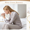 A woman is holding a mini cross rosary while sitting on a bed, with various styles of rosaries displayed nearby.