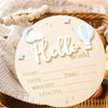 A light wood birth announcement sign with the word Hello and a cloud and hot air balloon design on a woven tray.