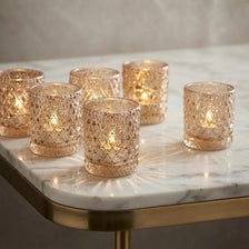 A collection of golden glass tealight candle holders arranged on a marble surface.