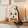 A light-colored wooden block carved into a face with large eyes and an open mouth, used as Halloween decor.
