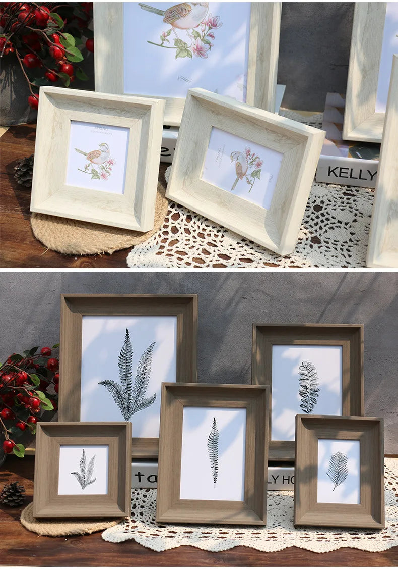 A collection of vintage resin photo frames in light wood and white displaying botanical prints on a rustic wooden surface.