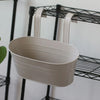 A modern boho metal hanging planter in off-white is displayed on a black wire shelf.