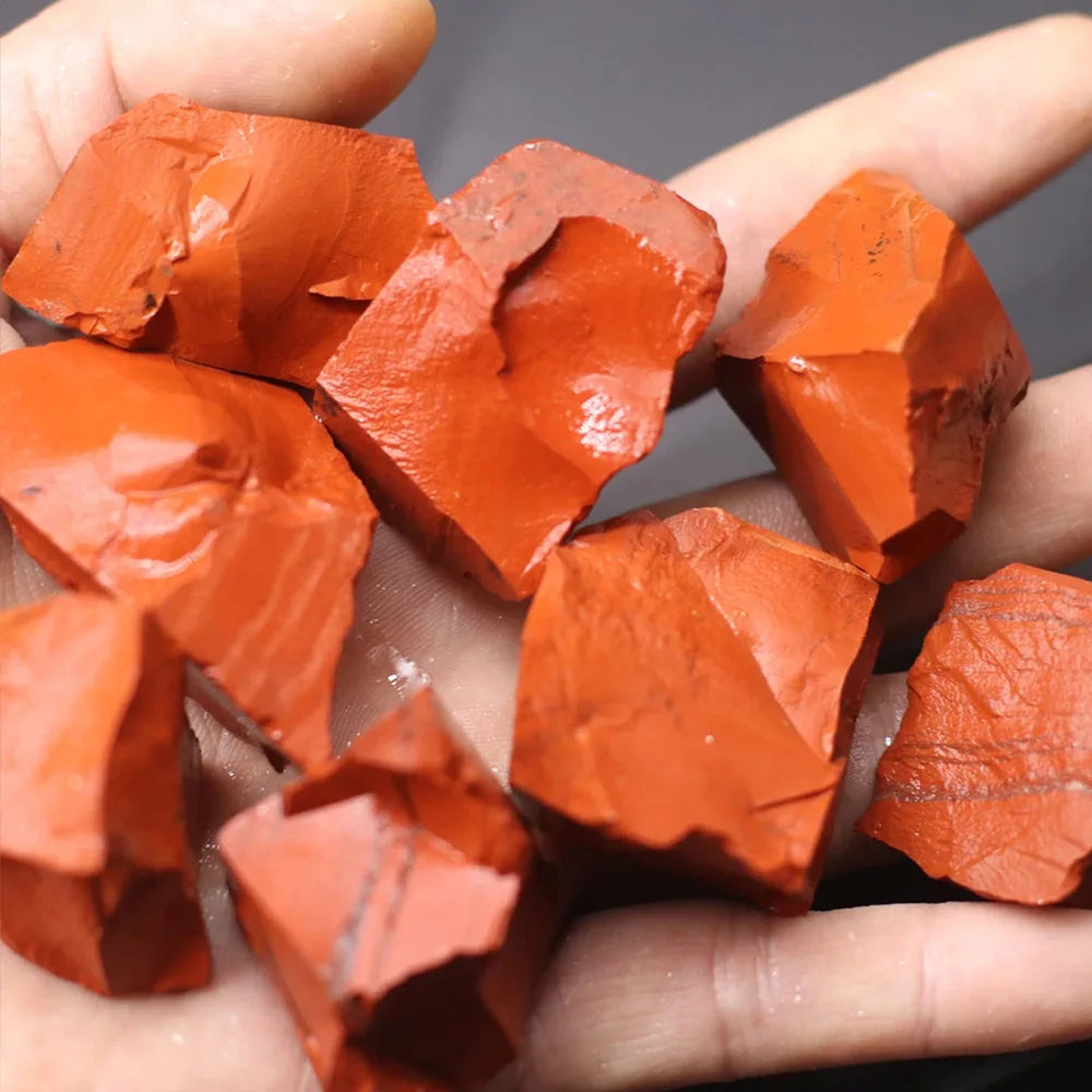 Several raw, reddish-orange crystal stones are held in a hand for display.