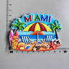 A colorful magnet featuring the word MIAMI, a beach scene with palm trees, and a striped umbrella.