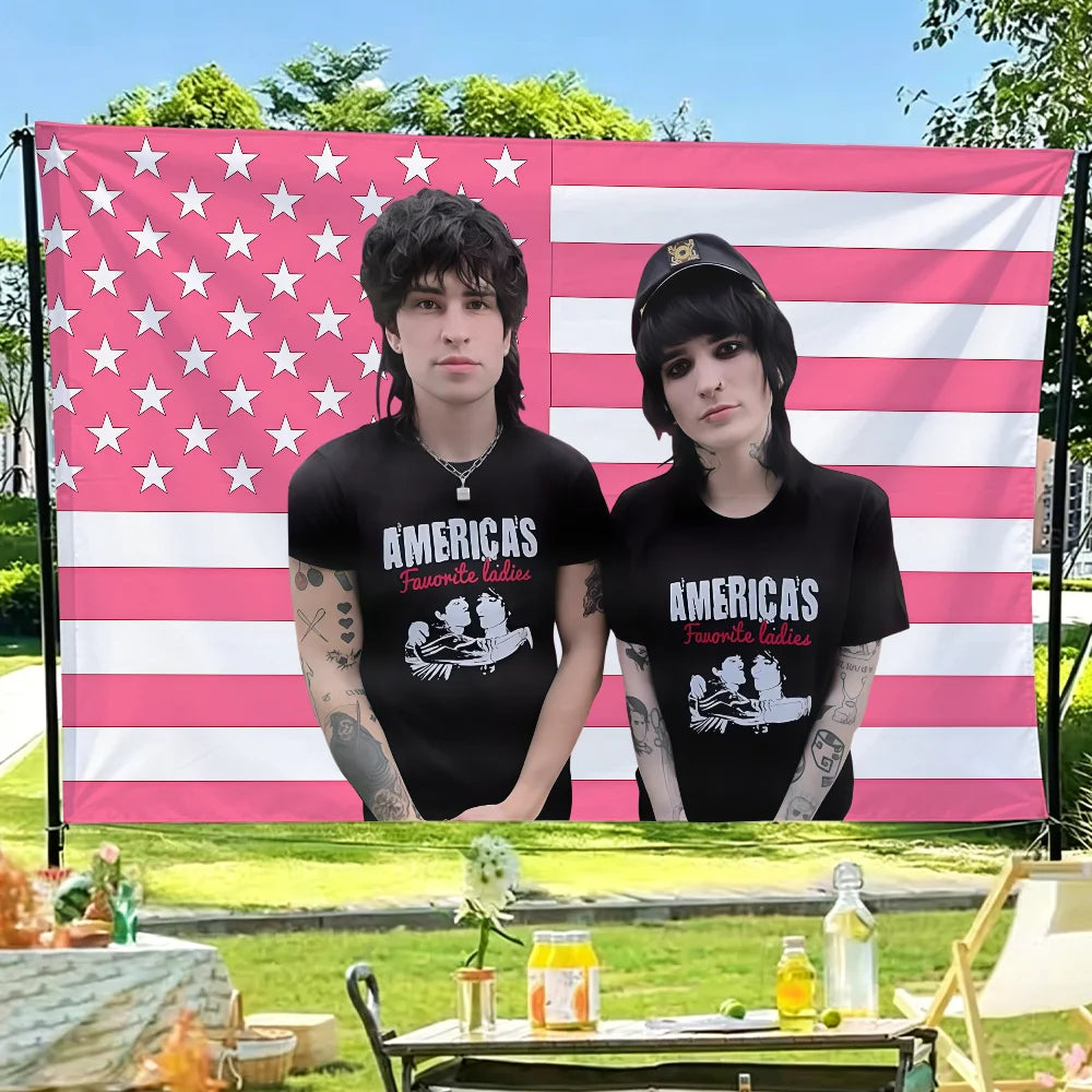 Two men in black t-shirts stand in front of an American flag backdrop.