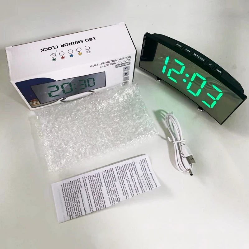 A black LED mirror clock with a digital display showing 12:03 and an accompanying power cord and packaging.