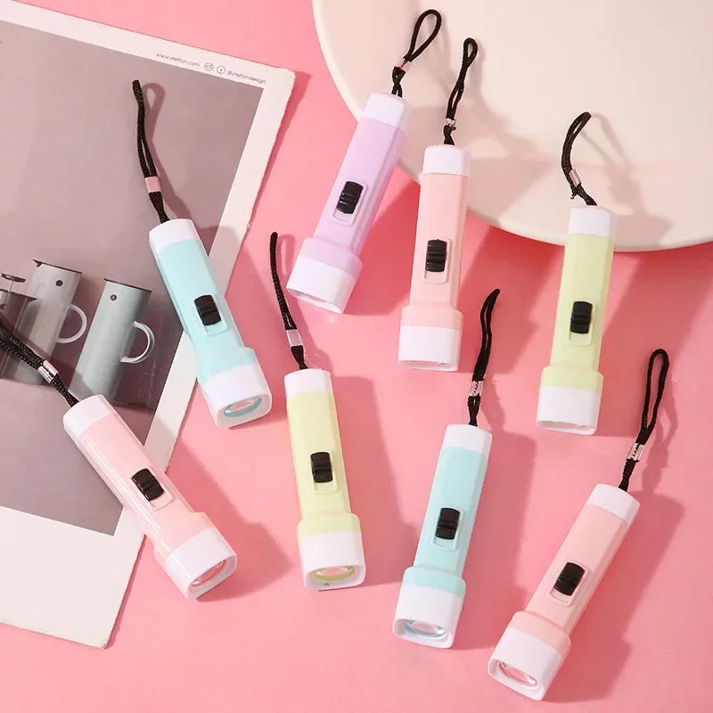 A collection of pink, mint green, and lime yellow compact pocket flashlights with black lanyards displayed on a pink backgrou