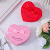 Red and pink heart-shaped gift boxes with ribbon and fresh roses displayed on a white surface