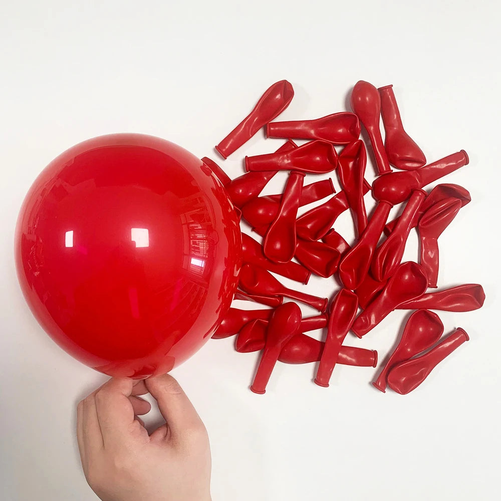 A hand holds a large red balloon and numerous red balloon shapes, including elongated pieces, against a white background.