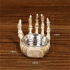 A white resin skull candle holder decoration with five fingers and a bowl, shown on a wooden surface.