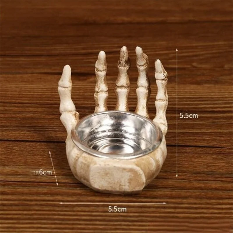 A white resin skull candle holder decoration with five fingers and a bowl, shown on a wooden surface.