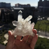 A hand holds a cluster of clear quartz crystals against an urban background.