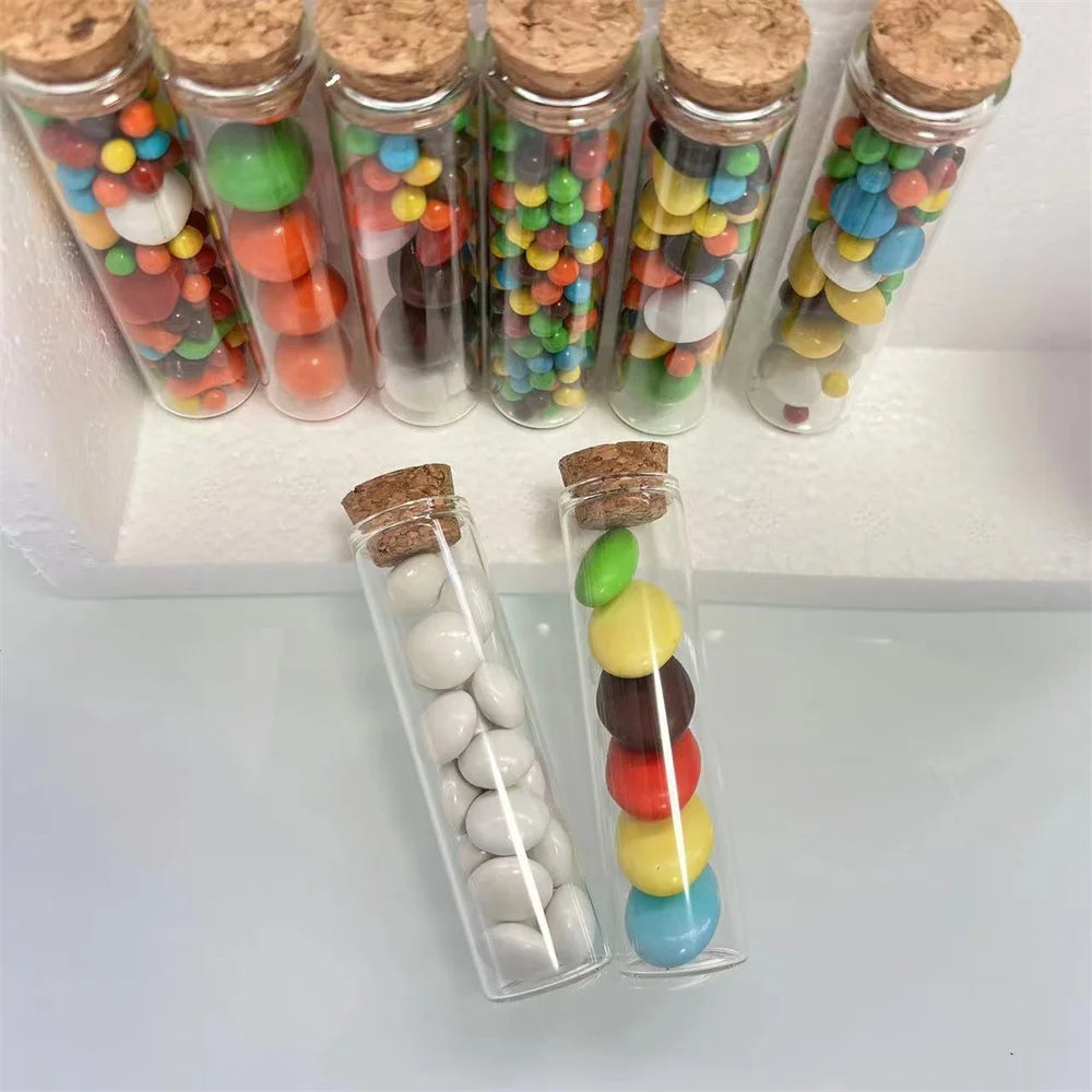 A collection of mini glass bottles filled with colorful candies and various colored glass beads, sealed with cork stoppers.