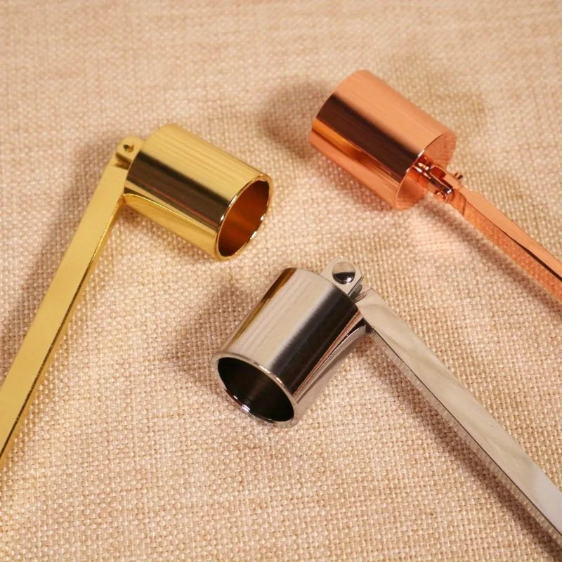 Three candle extinguisher tools in gold, copper, and stainless steel resting on a beige fabric.