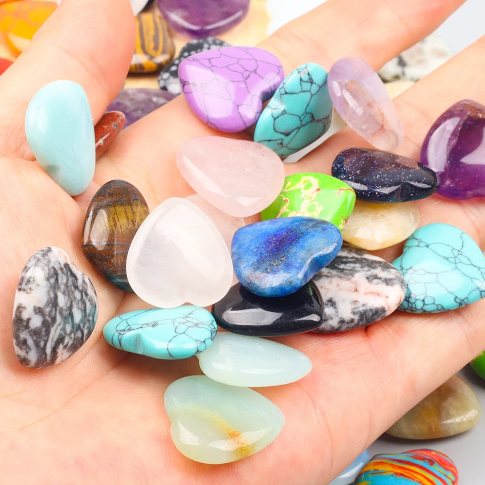 A hand holds a collection of heart-shaped amethyst and various colored crystal stones for healing and decor