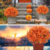 An orange artificial fall floral decor set featuring bright orange mums and carved pumpkins displayed outdoors.