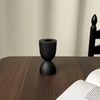 A black ceramic candle holder with a flared top and a round base, set against a wooden surface.