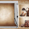 A photo show display featuring brown leather cowboy boots, a brown leather bag, and a brown hat against a rustic backdrop.
