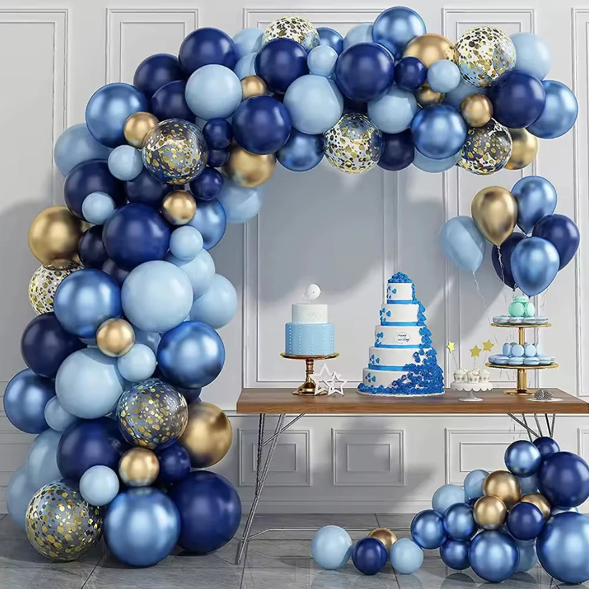 A balloon arch decoration featuring metallic blue and gold balloons with confetti, displayed against a light gray wall.