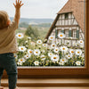 A child stands in front of a window decorated with white and yellow daisy flowers.