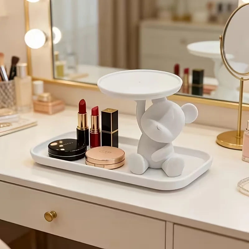 A white bear-shaped tray holding various makeup products and jewelry on a vanity surface.
