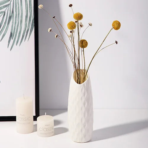 A white textured vase holds delicate dried flowers with thin stems and spherical yellow blooms.