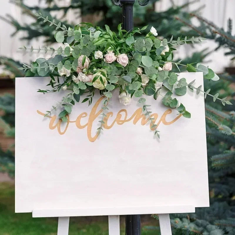 A sign with the words welcome decorated with green eucalyptus leaves and pink roses for home decor