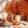 Un bouquet de fleurs artificielles d'automne et d'Halloween aux tons orange et rouille, présentées sur une table.